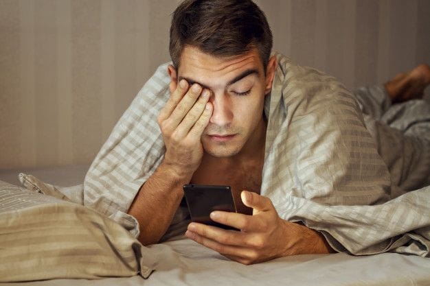 Premium Photo _ Closeup portrait sleepy young man messaging on smart phone in bed at home, suffering from insomnia